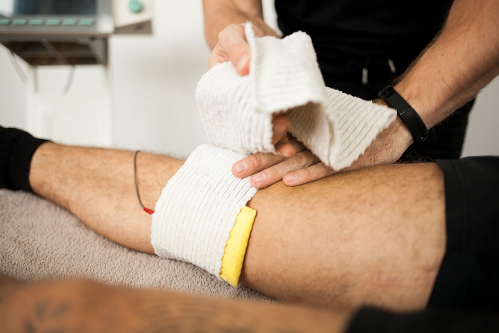 Ein Physiotherapeut bringt bei einem Patienten  Elektroden am Bein eines liegenden Patienten für die Elektrotherapie an