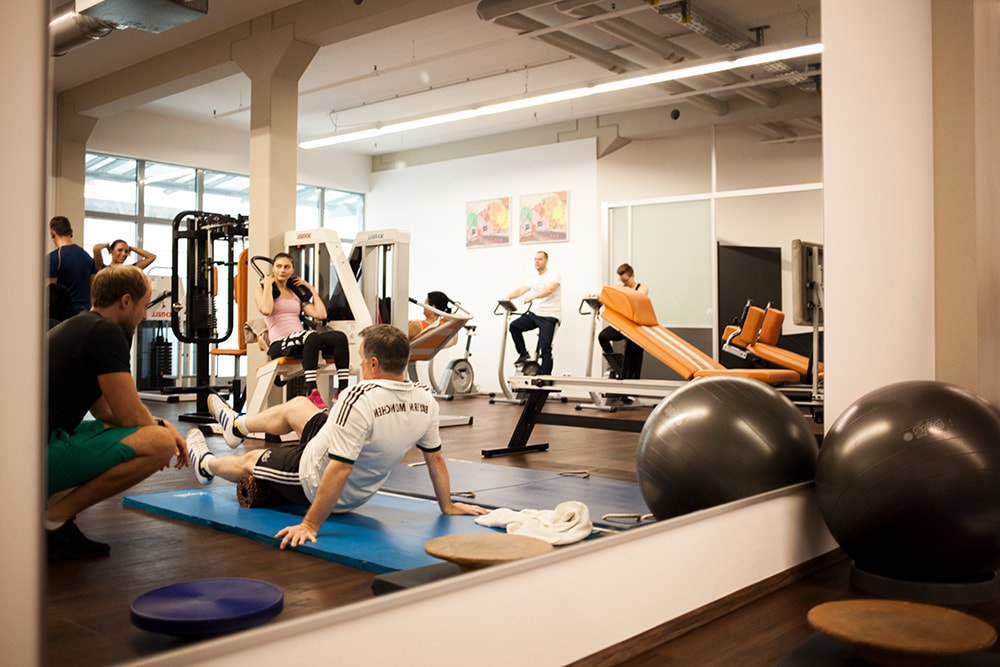 Großer Spiegel im Trainingsraum von PHYSICS Physiotherapie in Wasserburg, in dem sich mehrere Personen beim Training sowie ein Trainer widerspiegeln.