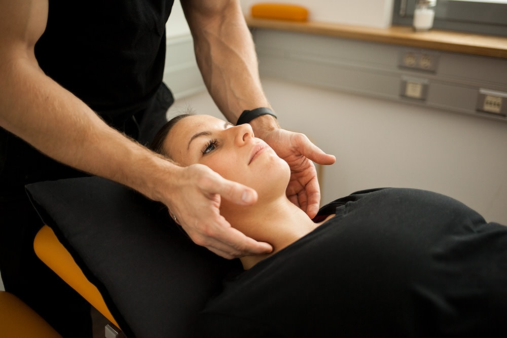 Eine Patientin wird liegend von einem Physiotherapeuten am Lymphsystem massiert