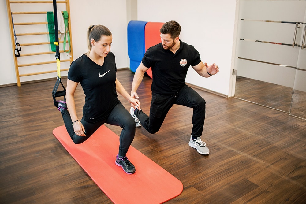 Ein Physiotherapeut übt mit einer Patientin einen Ausfallschritt am TRX Band
