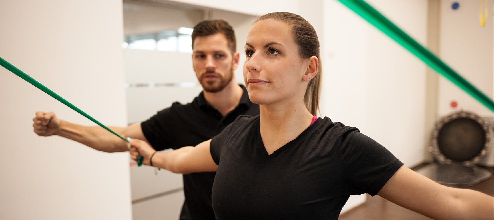 Physiotherapeut von Physics unterstützt eine Patientin beim Training mit TRX-Bändern im Trainingsraum.