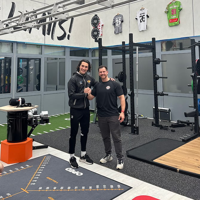 Der Inhaber von PHYSICS und der Cheftrainer der 360° Vision Academy reichen sich die Hände in einem Trainingsraum. Im Hintergrund sind Trainingsgeräte zu sehen.